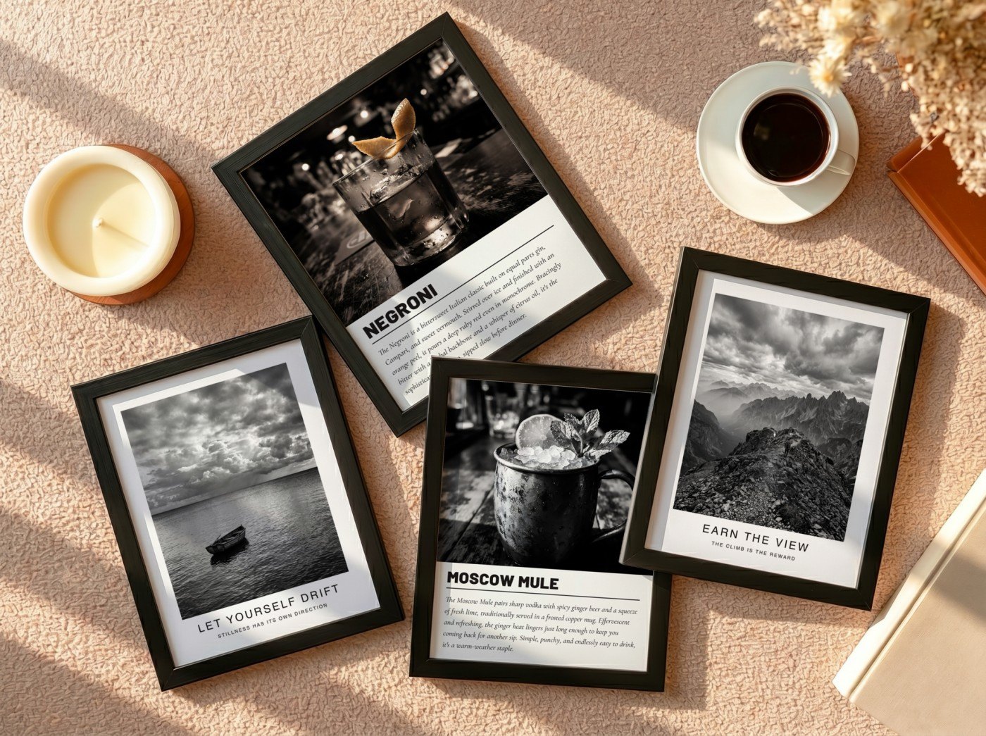 Four black frames in a flat lay on a beige carpet showing black and white prints: a mountain, a seascape with a boat, a Negroni cocktail and a Moscow Mule