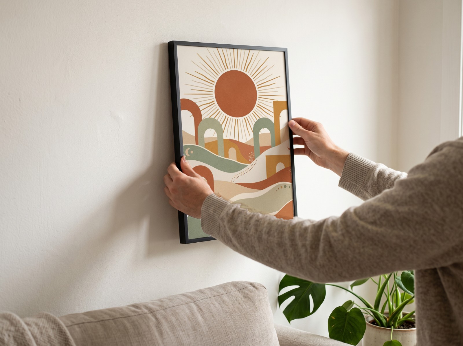 Black Frame Being Hung on a White Living Room Wall showing a boho sun wall art