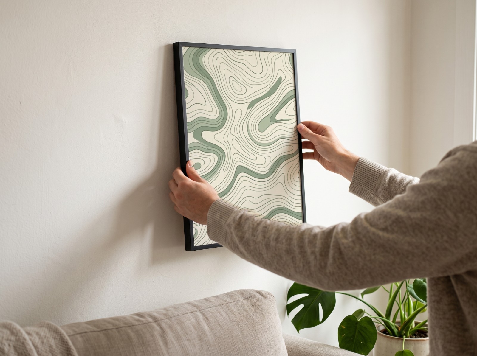 Black Frame Being Hung on a White Living Room Wall showing a sage topographic map pattern