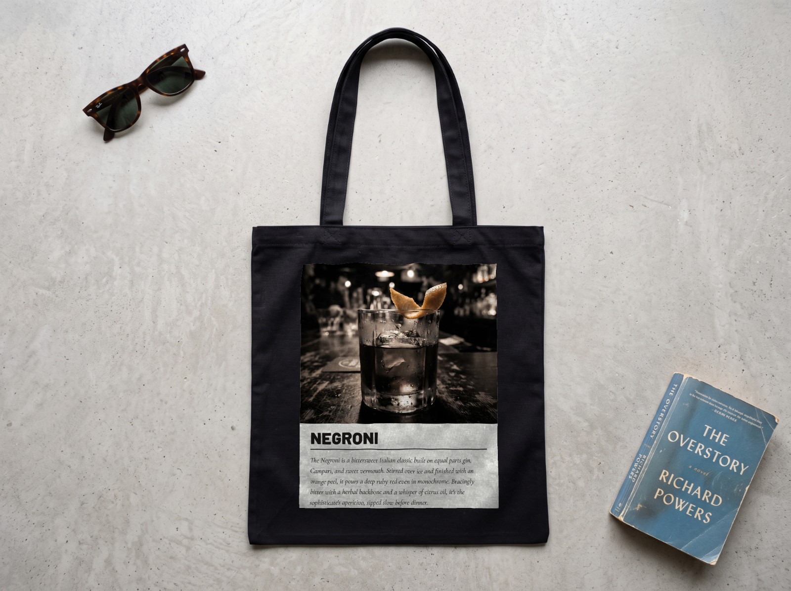Black Tote Bag Flat Lay on Concrete showing a Negroni cocktail print