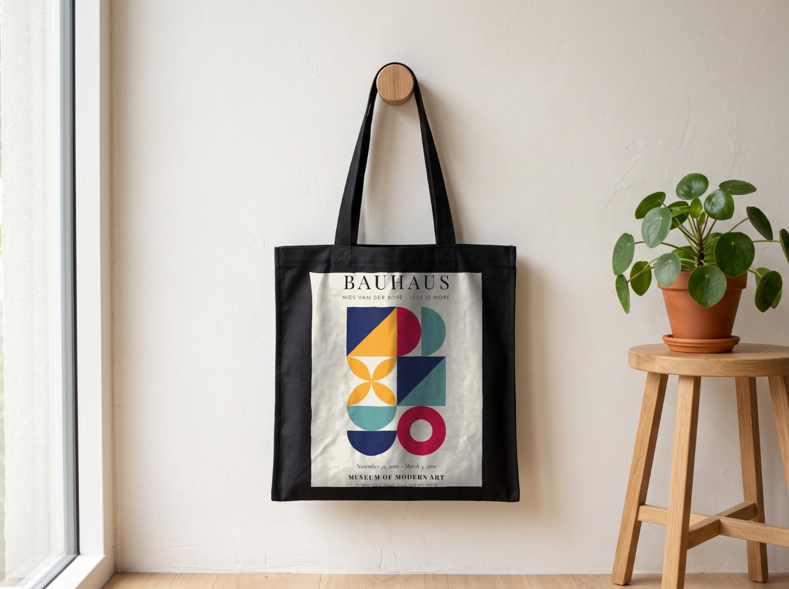 Black Tote Bag on a Wooden Wall Peg showing a Bauhaus Less is More print