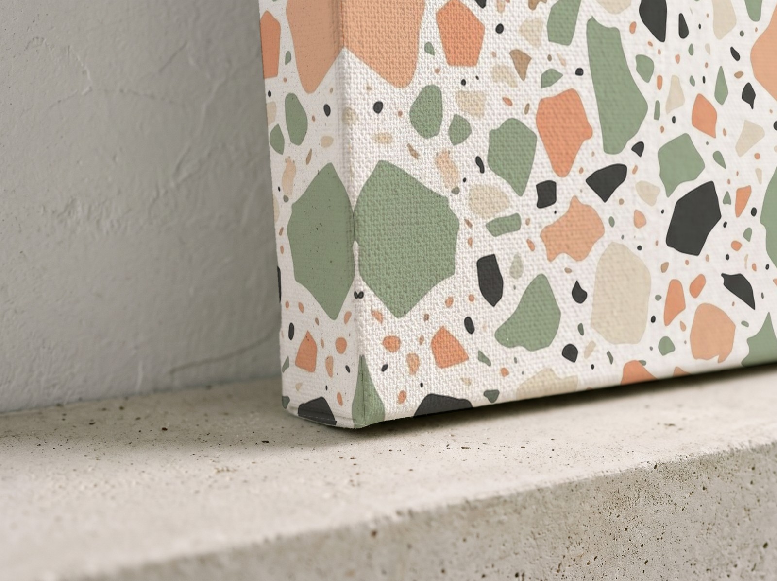 Corner close-up of a textured mirror edge canvas with a terrazzo print on a concrete shelf