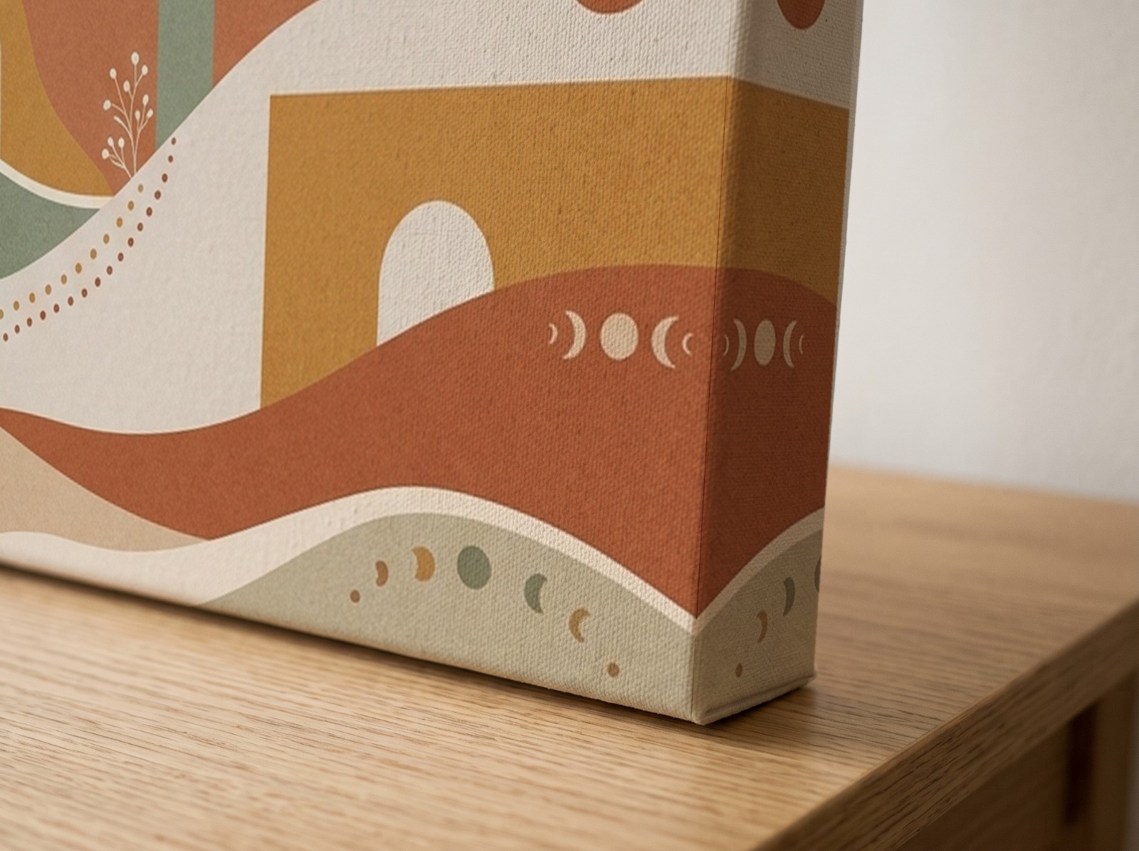 Corner close-up of a textured mirror edge canvas with a boho sun print on an oak table