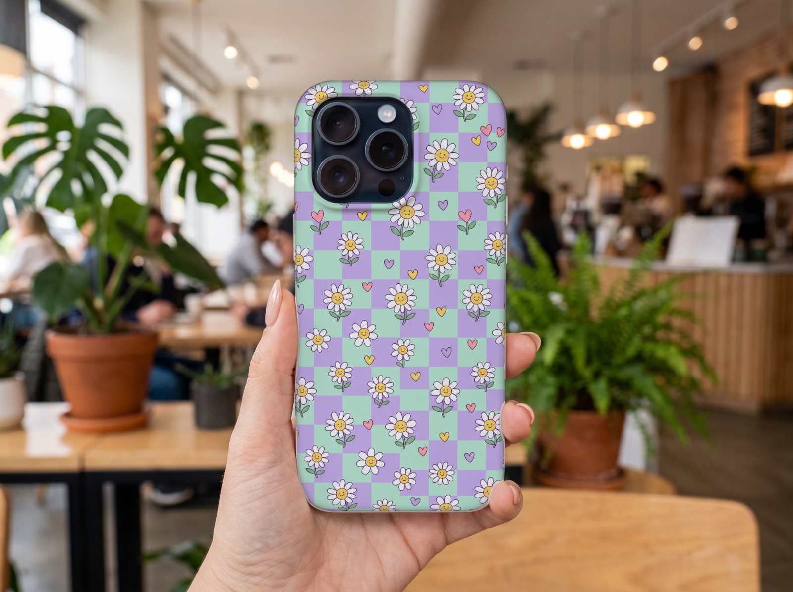 iPhone 15 Pro Case Held in a Hand in a Café showing a pastel checkerboard daisy print