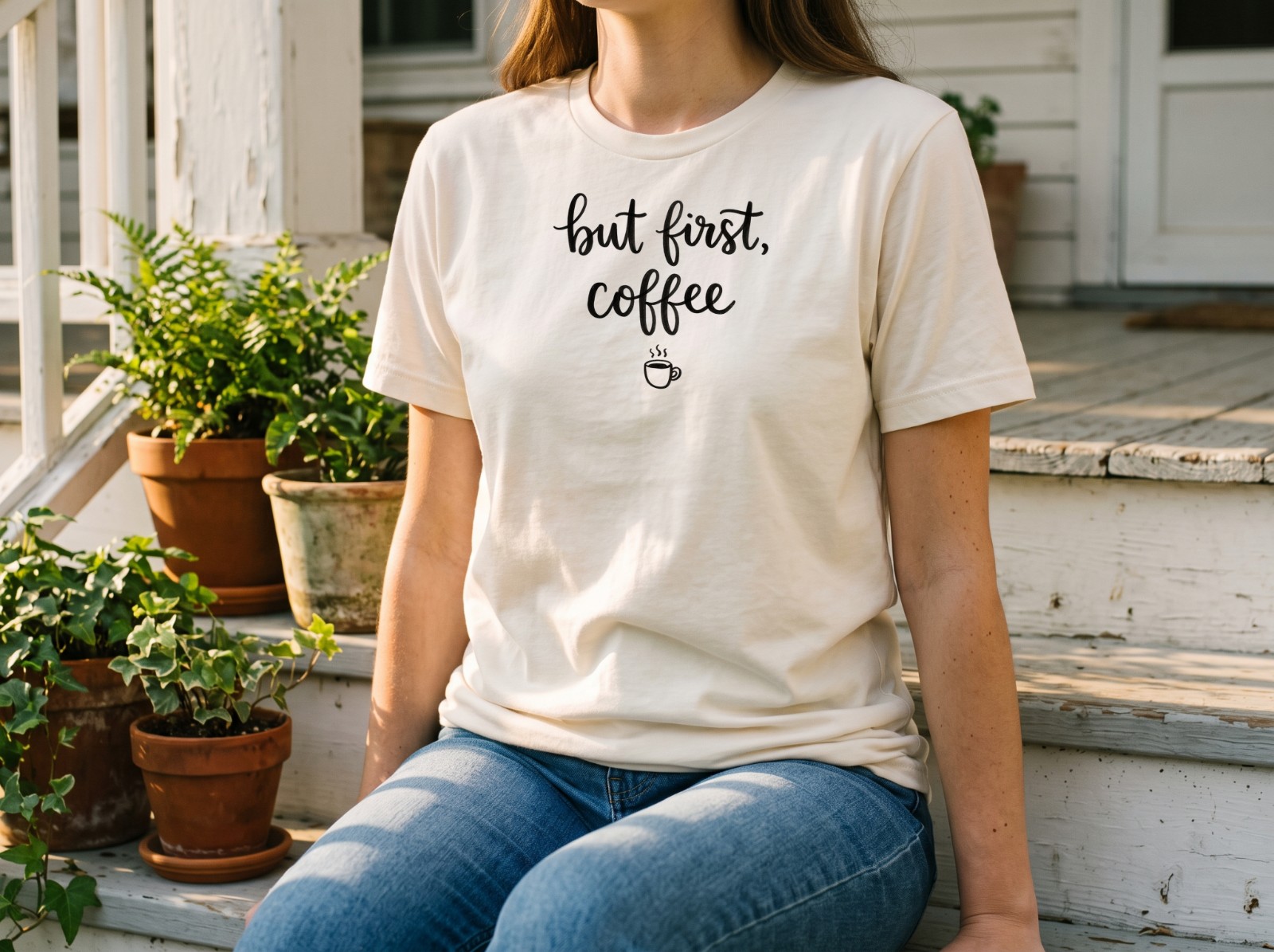 Natural T-Shirt on a Woman Sitting on Porch Steps showing a But First Coffee lettering design