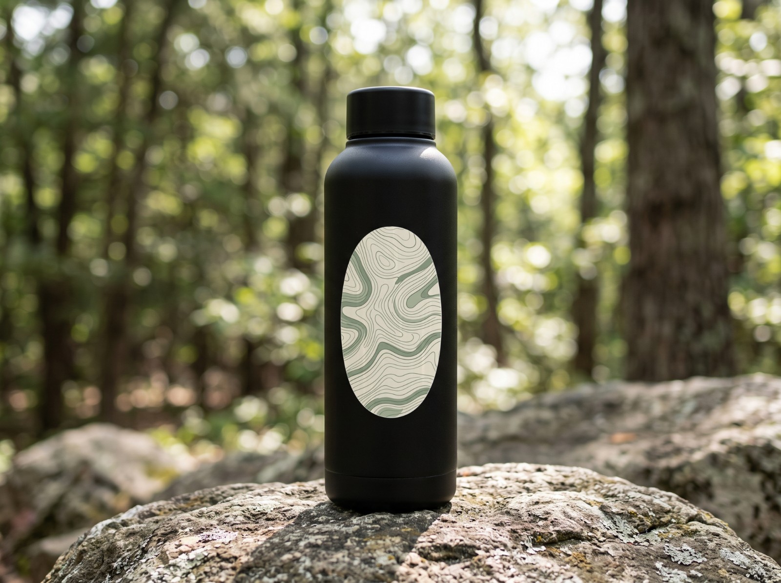 Oval Vinyl Sticker on a Black Water Bottle in a Forest showing a sage topographic map pattern