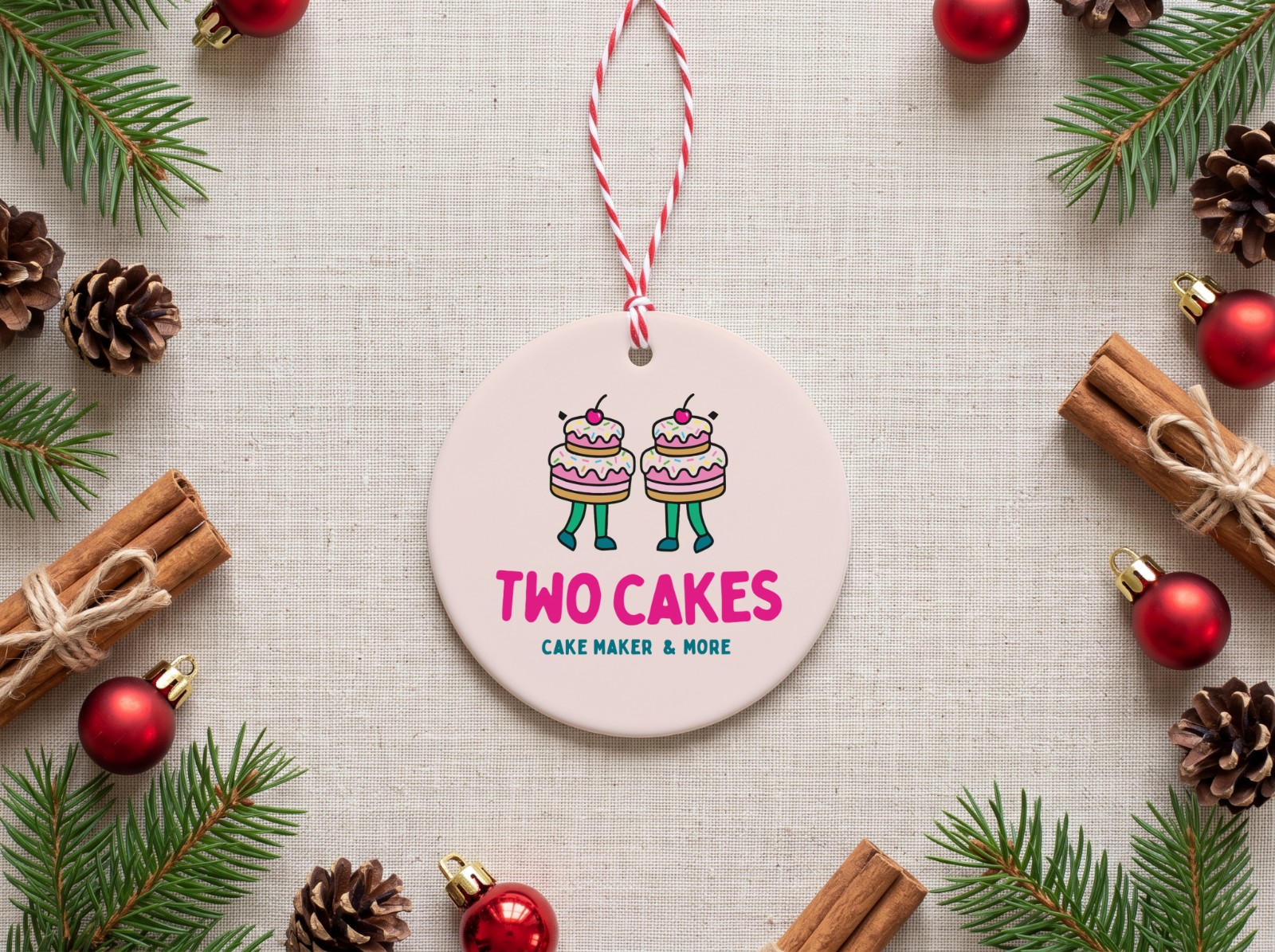 Round Ceramic Christmas Ornament Flat Lay with Pine showing the Two Cakes logo