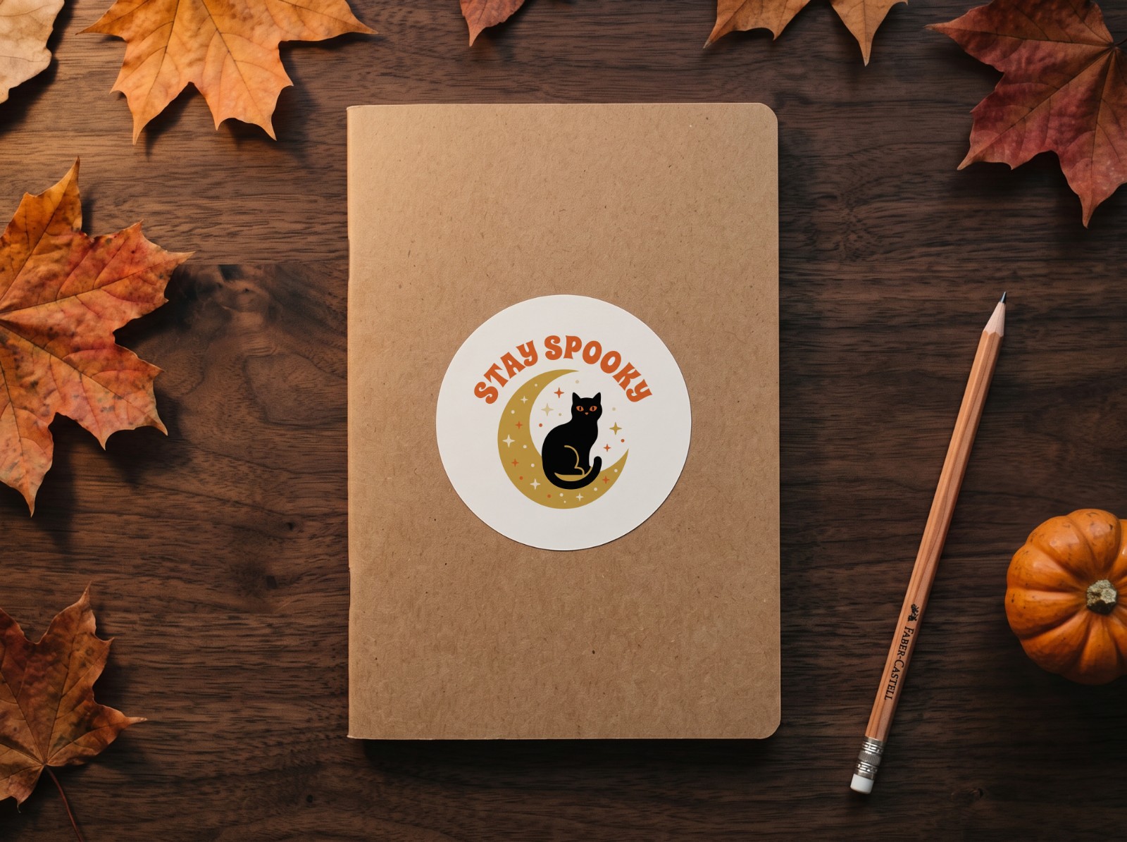 Round Sticker Halloween on a Kraft Notebook with Autumn Leaves showing a Stay Spooky black cat and moon design