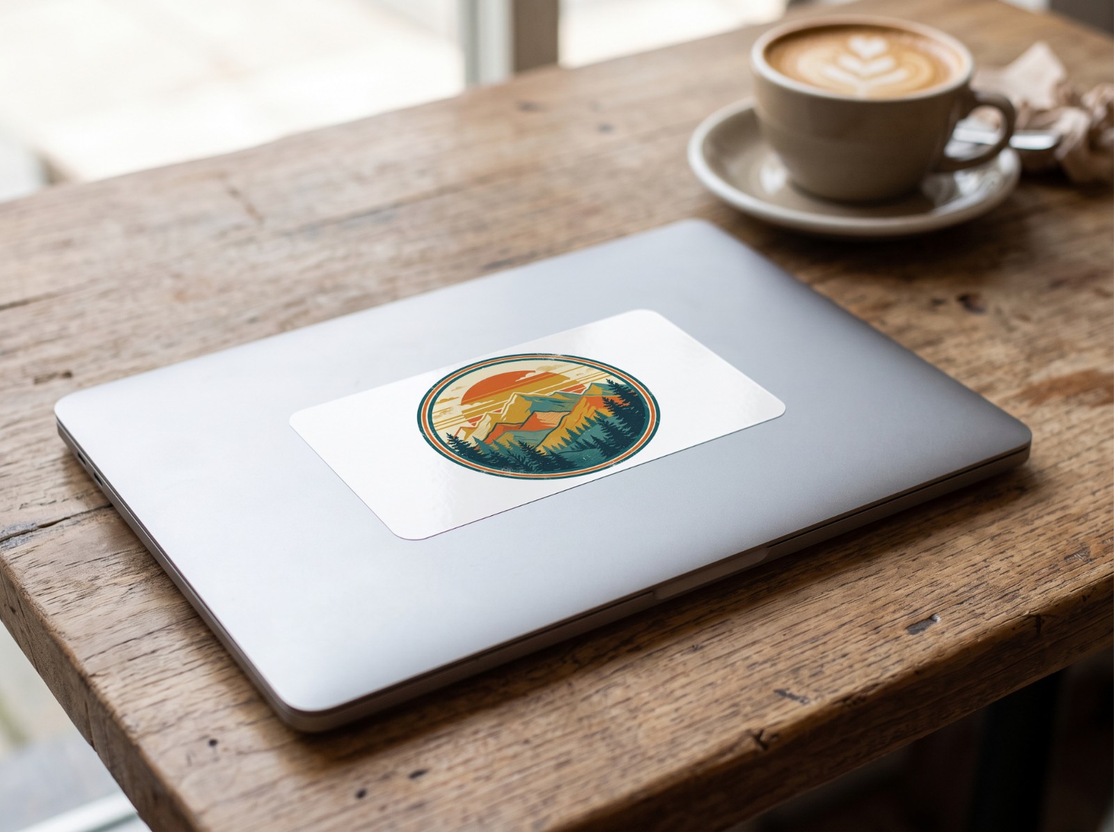 Vinyl Sticker on a Laptop Lid in a Cafe showing a retro mountain sunset badge