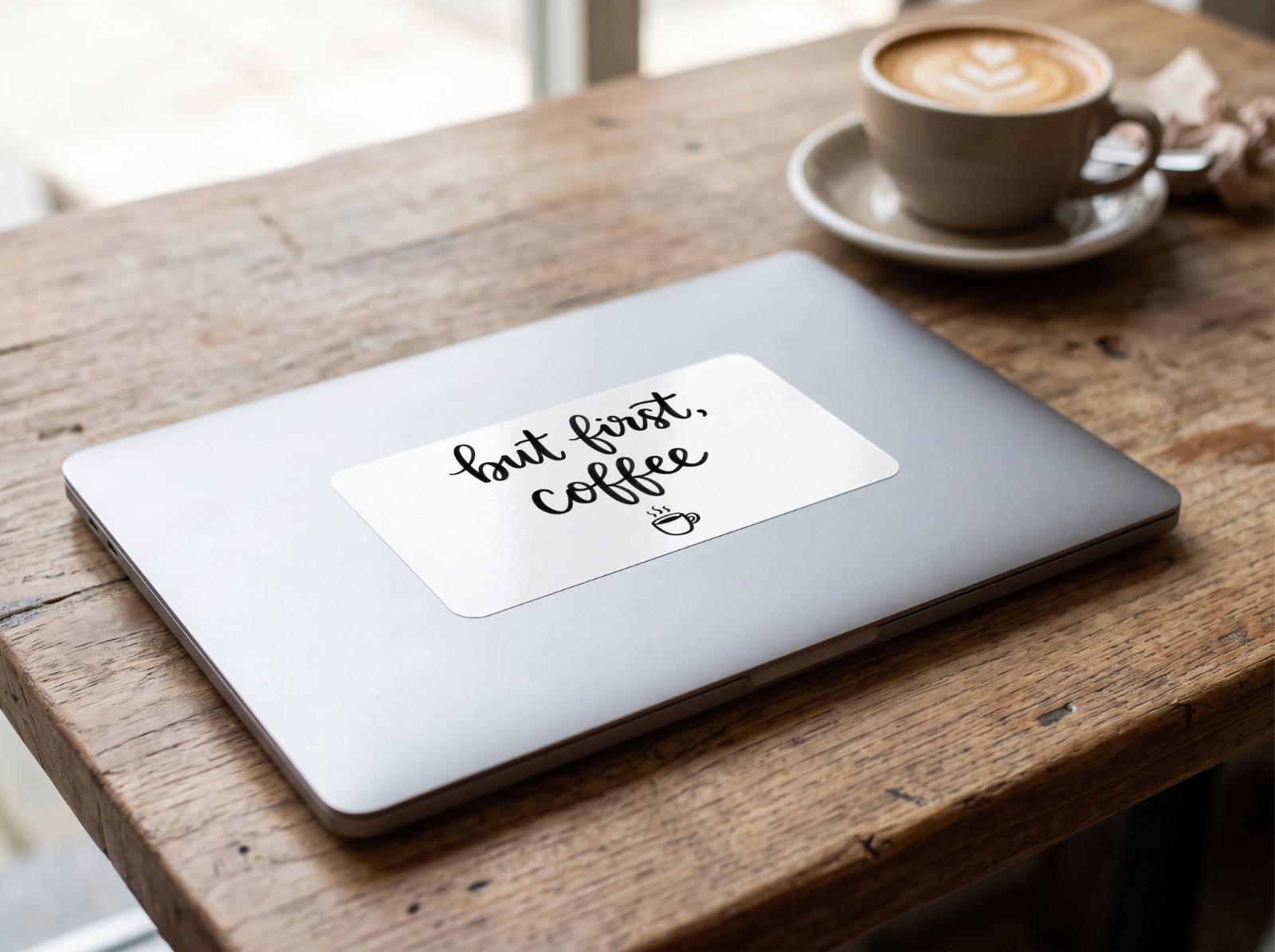 Vinyl Sticker on a Laptop Lid in a Cafe showing a But First Coffee lettering design