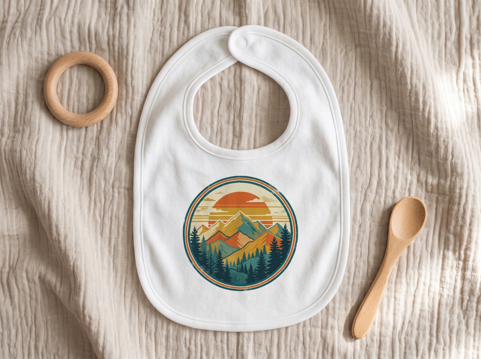 White Baby Bib Flat Lay on Muslin with a Teether showing a retro mountain sunset badge