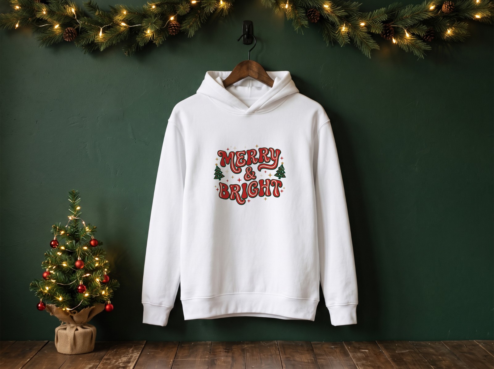 White Hoodie Christmas Mockup on a Hanger with a Green Wall and Garland example