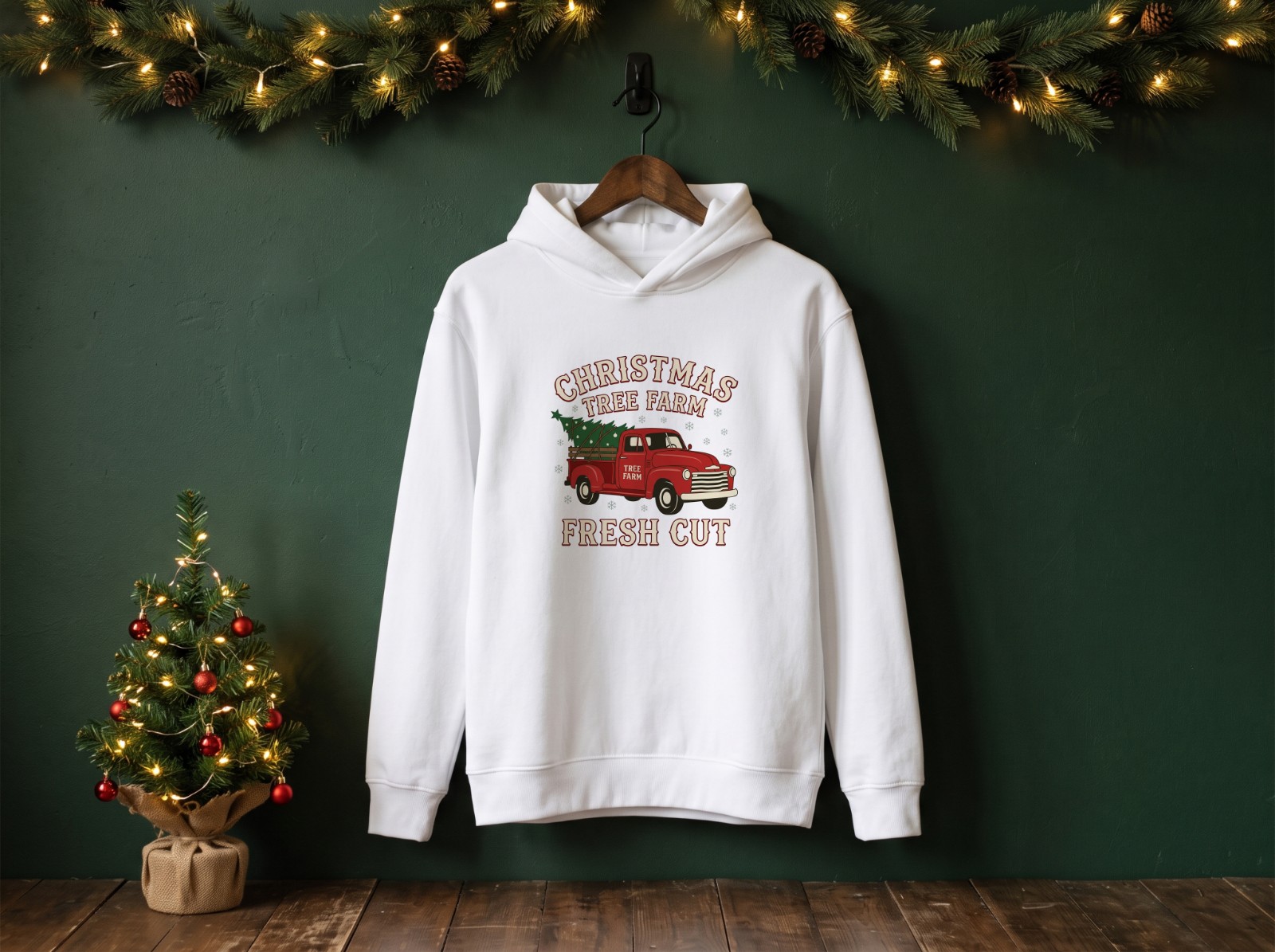 White Hoodie Christmas on a Hanger with a Green Wall and Garland showing a vintage Christmas tree farm truck design