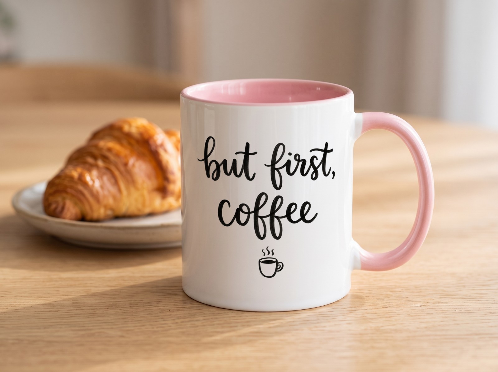 Pink Accent Mug on an Oak Table with a Croissant showing a But First Coffee lettering design