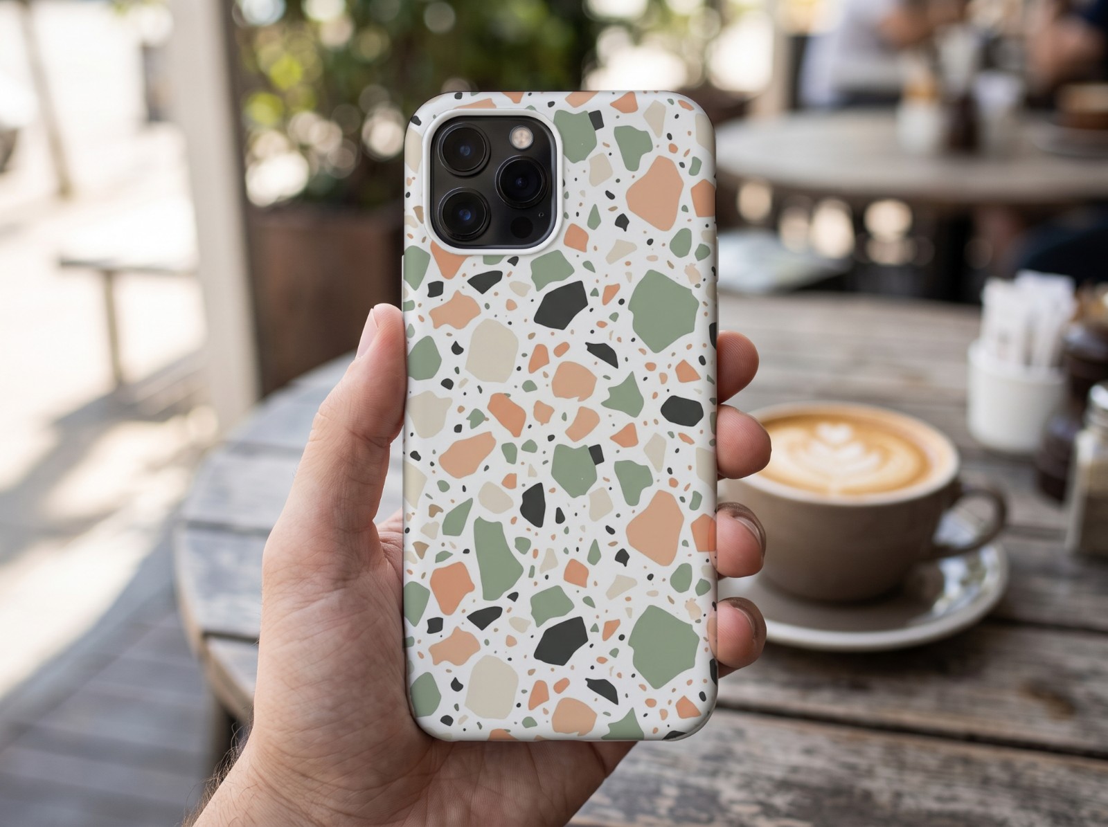 White Phone Case Held in a Hand at a Cafe showing a pastel terrazzo pattern
