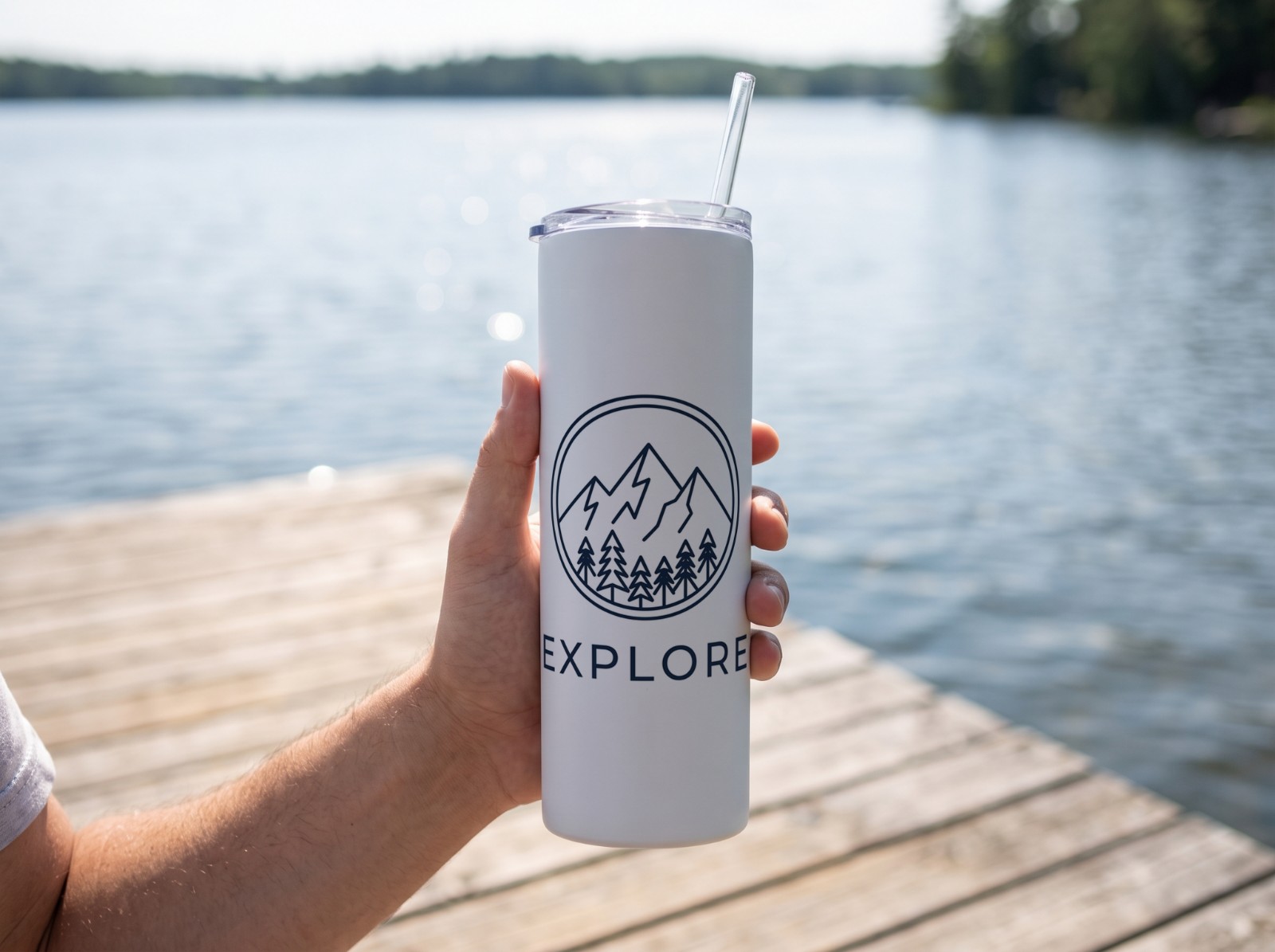 White Skinny Tumbler Held in a Hand on a Lake Dock showing an Explore mountain emblem