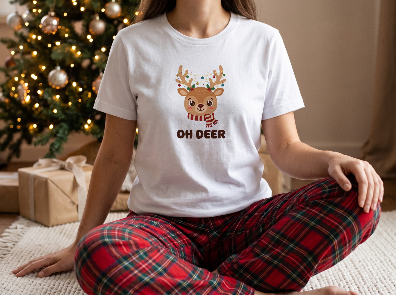 White T-Shirt on a Woman by a Christmas Tree in Plaid Pyjamas showing an Oh Deer reindeer design