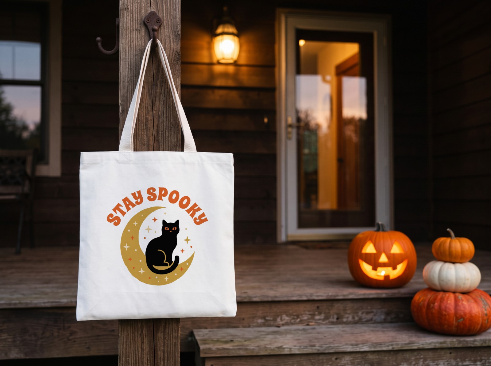 White Tote Bag Halloween on a Porch with a Jack-o'-Lantern showing a Stay Spooky black cat and moon design
