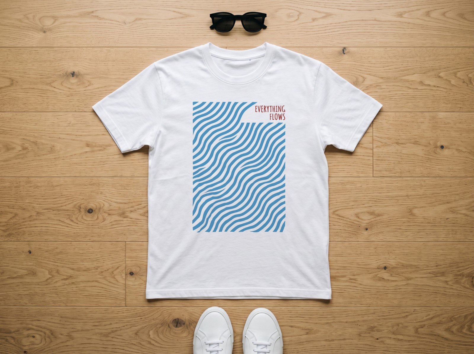 White T-Shirt Flat Lay on an Oak Floor showing an Everything Flows wave print