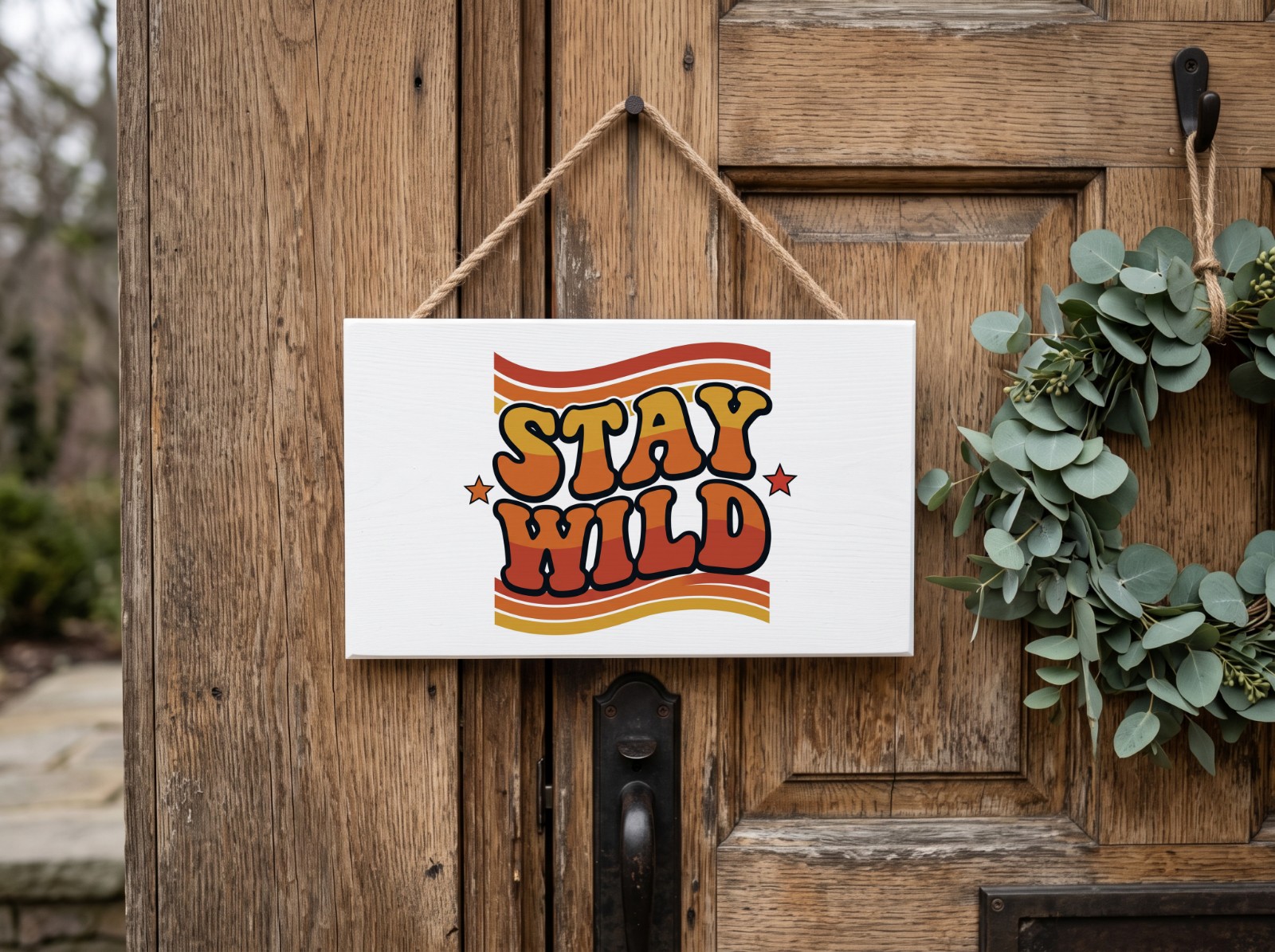 White Wooden Sign on a Rustic Door with a Wreath showing the retro Stay Wild design